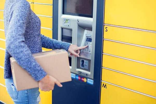 Woman client using automated self service post terminal machine or locker to deposit the parcel for storage,
