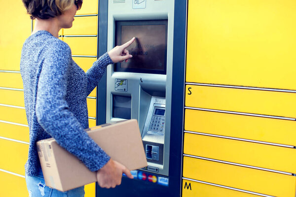 Woman client using automated self service post terminal machine or locker to deposit the parcel for storage,