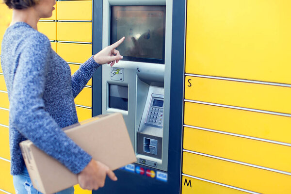 Woman client using automated self service post terminal machine or locker to deposit the parcel for storage,