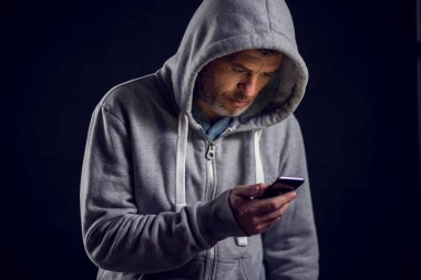 Kapüşonlu kazaklı adam telefonu elinde tutuyor. İnsanlar ve alet konsepti