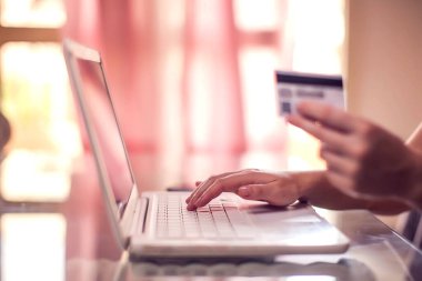 Kadının elinde kredi kartı var ve bilgisayarla online ödeme yapıyor. Çevrimiçi alışveriş ve teknoloji kavramı