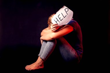 Kadın, siyah arka planda kendisine yardım etmesi için elinde mesajla kâğıt tutuyor. İnsanlar, aile içi şiddet, suç kavramı