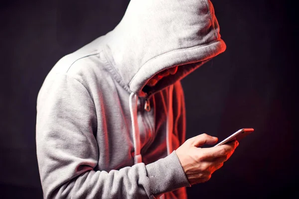 Elinde cep telefonu olan kapüşonlu kazak giyen bir adam. Suç ve hack kavramı