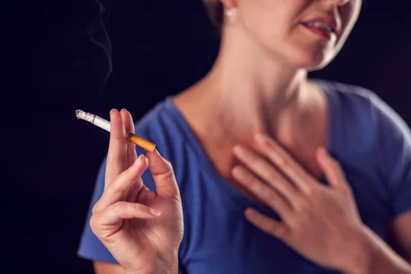 Woman smokes cigarette and has lungs or heart pain on black background. Tobacco addiction and health problem concept