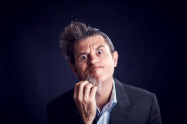 Yarı sakallı, takım elbiseli, siyah arka planda yüzünü tırmalayan komik bir adam. İnsan ve cilt bakımı kavramı