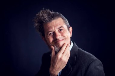 Yarı sakallı, takım elbiseli, siyah arka planda yüzünü tırmalayan komik bir adam. İnsan ve cilt bakımı kavramı