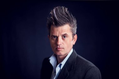 Mohawk saçlı bir adam siyah arka plan önünde takım elbise giyiyor.. 