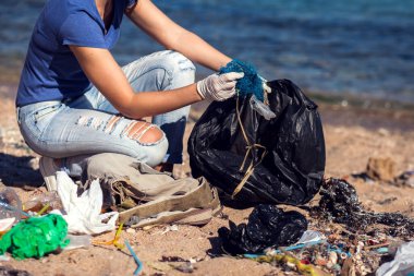 Siyah çantalı bir gönüllü kumsalda çöp topluyor. Çevre kirliliği kavramı
