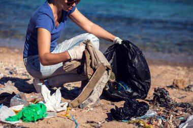 Siyah çantalı bir gönüllü kumsalda çöp topluyor. Çevre kirliliği kavramı