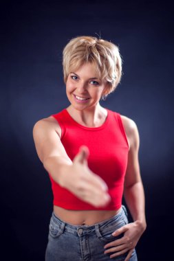 Kısa sarı saçlı, kırmızı gömlekli genç bir kadın portresi. Siyah arka planda kameraya el sıkışırken görülüyor. İnsanlar, duygular ve davetkar kavramlar