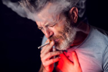 Adam sigara içiyor ve siyah arka plandaki akciğerlerle sorunu var. Sigara bağımlılığı konsepti