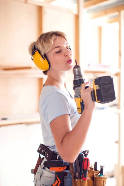 Handy woman with short hair with headphones working with drill.