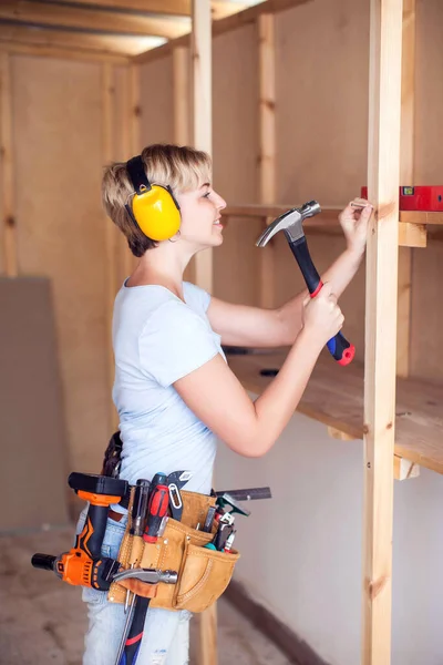 Handy woman with short hair with headphones working with hammer.