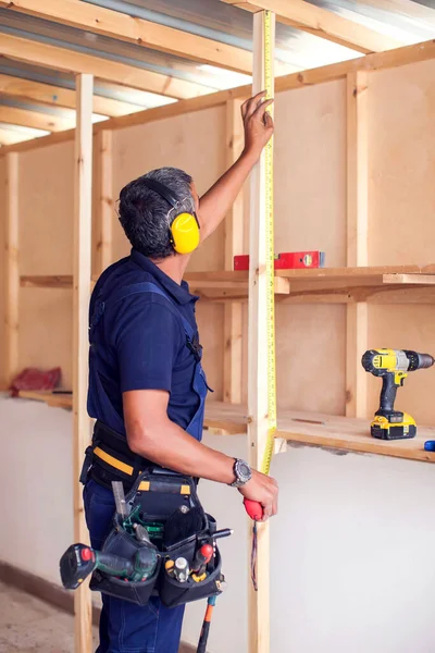 Handyman with yellow headphones works with building tape does repair.