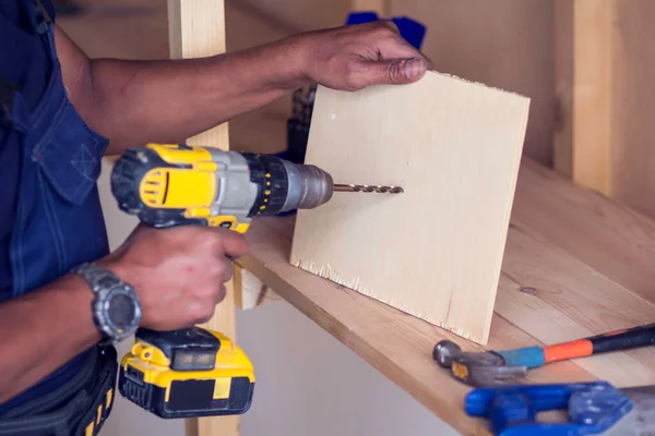 Handyman with yellow headphones works with drill does repair.