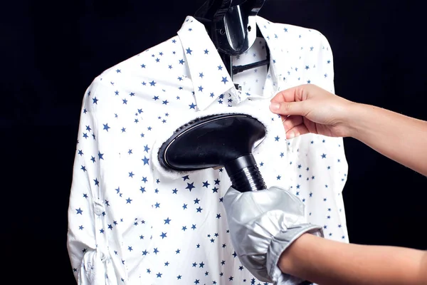 Woman steaming blouse in front of black background. Hausework, lifestyle concept