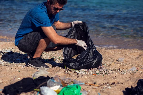 가방을 자원하는 사람이 해변에서 쓰레기를 모은다 — 스톡 사진