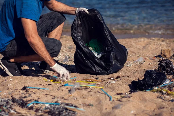 黒い袋を持った男ボランティアが海岸にゴミを集める 環境汚染の概念 — ストック写真