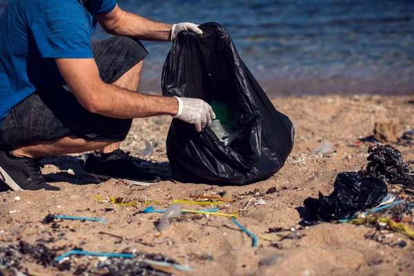 黒い袋を持った男ボランティアが海岸にゴミを集める 環境汚染の概念 — ストック写真