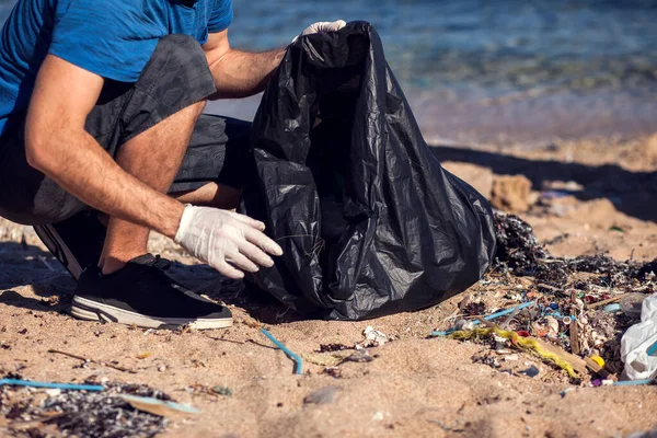 带着黑包的志愿者在海滩上捡垃圾 环境污染概念 — 图库照片