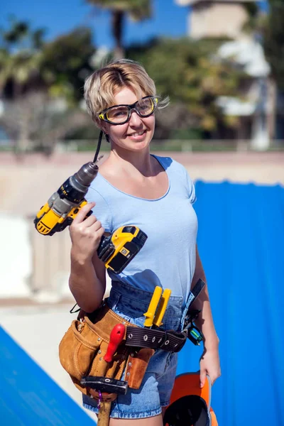 Handy woman with toolsbelt and yellow drill in her hands outdoors