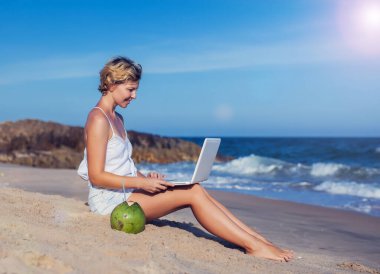 Sahilde dizüstü bilgisayarı olan, arkasında deniz olan güzel, sıradan bir kadın.