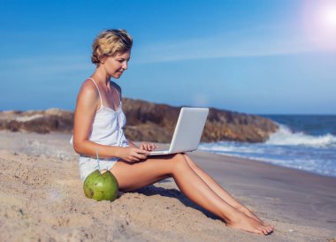 Sahilde dizüstü bilgisayarı olan, arkasında deniz olan güzel, sıradan bir kadın.