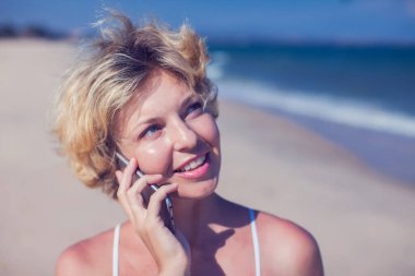 Deniz altyapısı olan bir sahilde cep telefonuyla konuşan mutlu genç bir kadın.