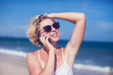 Deniz altyapısı olan bir sahilde cep telefonuyla konuşan mutlu genç bir kadın.