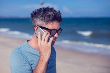 Genç adam sahilde akıllı telefon kullanıyor.