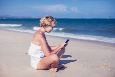 Deniz altyapısı olan bir sahilde cep telefonuyla konuşan mutlu genç bir kadın.