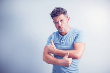 Orta yaşlı bir adam, mavi arka planda izole edilmiş, kameraya olumlu bir hareket, hoşlanma ve onaylama ifadesi göstererek gülümsüyor.