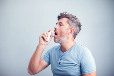 Boğaz ağrısı için sprey sıkın. Boğazına sprey sıkan ve ağzına serpiştiren bir adamın fotoğrafı. Sağlık ve hastalık kavramı.