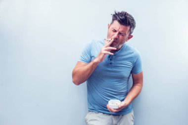 Gri arka planda, kahverengi saçlı, gömlek giyen yakışıklı bir genç. Sigara içiyorum..