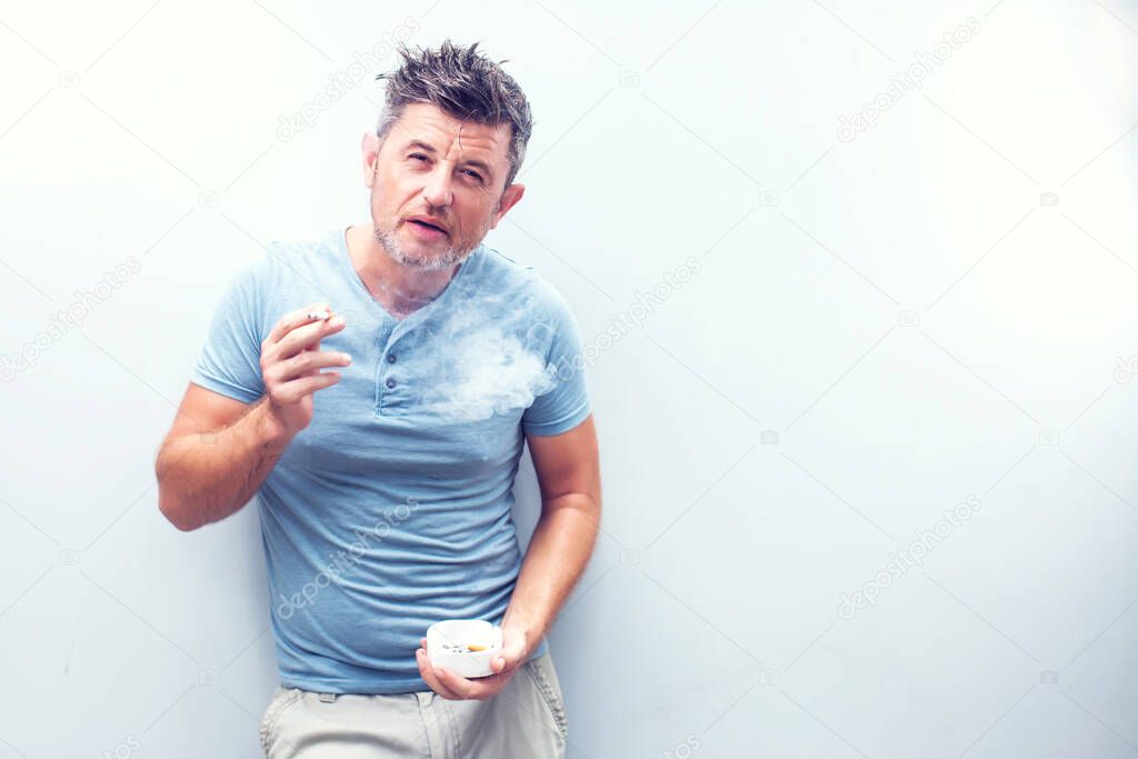 Handsome young man with brown hair wearing shirt isolated on grey background. Smoking cigarette.