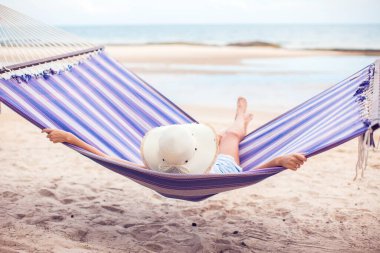 Kumsalda hamakta oturan şapkalı kadın. Seyahat ve tatil kavramı.
