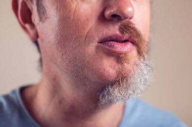 Kahverengi arka planda yarım sakallı ve saçlı bir adam portresi.