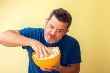 Sarı arka planda patlamış mısır yiyen komik bir adamın portresi.