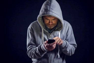 Kapüşonlu kazaklı adam telefonu elinde tutuyor. İnsanlar ve alet konsepti
