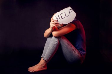 Kadın, siyah arka planda kendisine yardım etmesi için elinde mesajla kâğıt tutuyor. İnsanlar, aile içi şiddet, suç kavramı