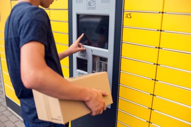 Man client using automated self service post terminal machine or locker to deposit a parcel for storage clipart