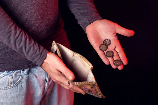 Man shows empty wallet and coins in hand in front of black background. Poverty and financial problems concept