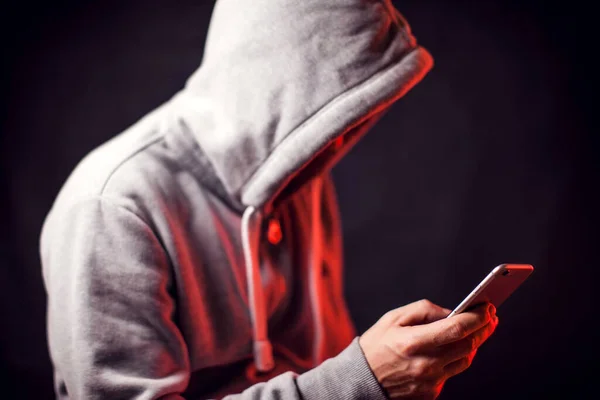Elinde cep telefonu olan kapüşonlu kazak giyen bir adam. Suç ve hack kavramı