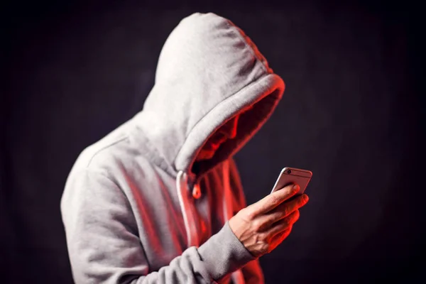 Elinde cep telefonu olan kapüşonlu kazak giyen bir adam. Suç ve hack kavramı