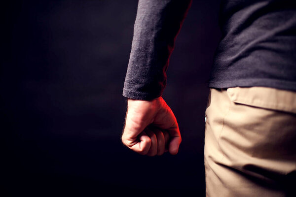 Man shows fist in front of black background. People, family violence, crime concept