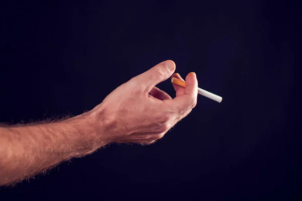 Cigarette in hand on black background. Smoke addiction concept