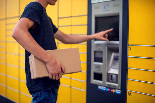 Man using automated self service post terminal machine or locker to deposit the parcel for storage