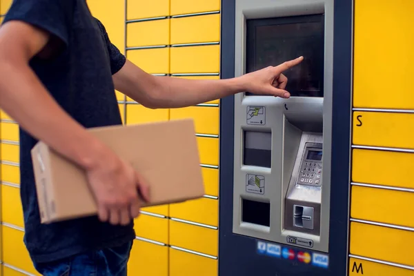 Man using automated self service post terminal machine or locker to deposit the parcel for storage