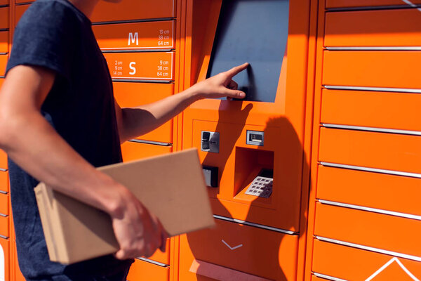Man using automated self service post terminal machine or locker to deposit the parcel for storage