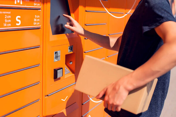 Человек с помощью автоматического самообслуживания почтового терминала или шкафчика для хранения посылки